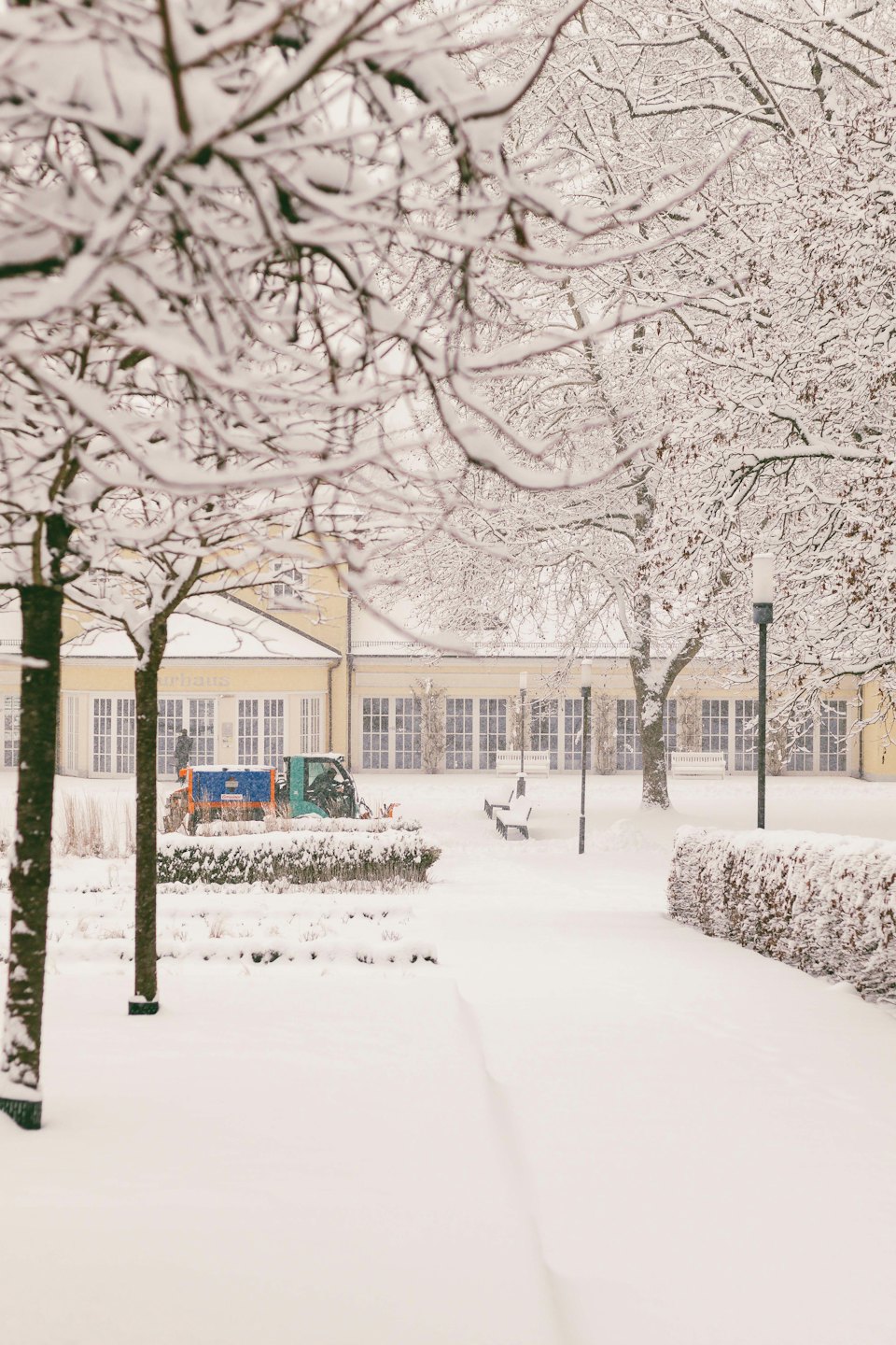 Groundskeeper clears snow from a path near a yellow building.